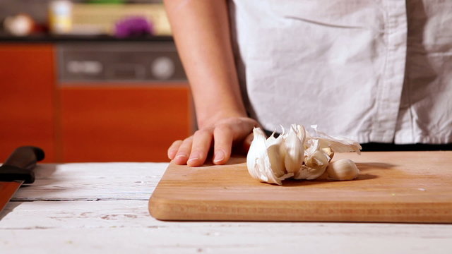 Woman crushed the garlic head with hand on the wooden cutting board