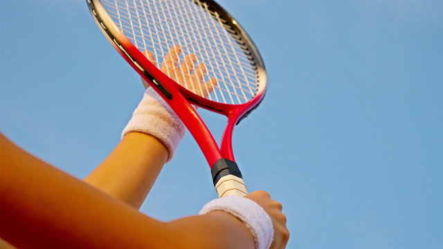 tennis player's hand hitting the net of her tennis racket against blue sky
