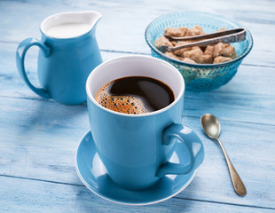 Cup of coffee, milk jug and cane sugar cubes.