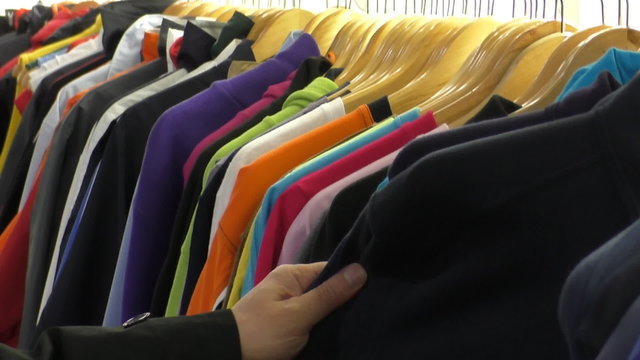 Variety of colourful t-shirts hanging on wooden hangers at the clothes shop, man chooses one casual top