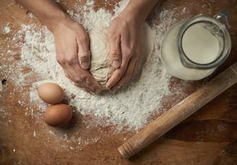 Close-up of baker hands kneading cake dough on the board with flour, eggs and milk. Baking concept. - obrazy, fototapety, plakaty