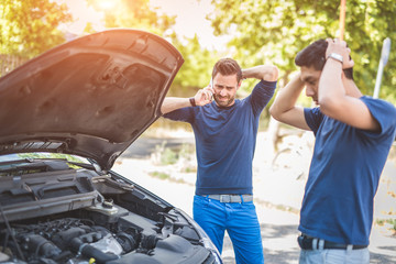 Friends examining broken down car on sunny day