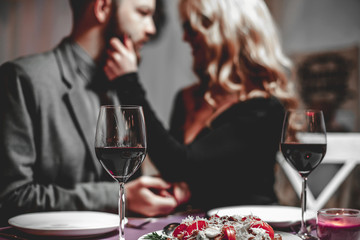 Beautiful young couple with glasses of red wine in luxury restaurant
