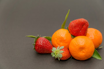 Fototapeta na wymiar strawberries and Three tangerine with leaves on a beautiful gray background, beautiful colors and composition