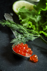 Red salmon caviar in a silver spoon on a black stone background
