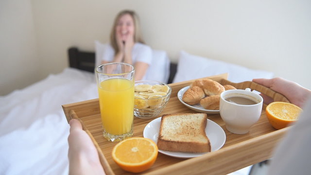 Hands holding breakfast tray for happy woman.