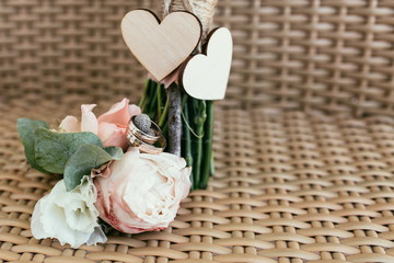 wedding rings with pink roses against two wooden hearts