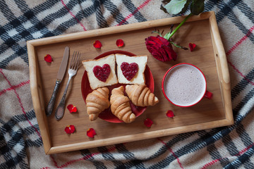 Valentines day romantic breakfast in bed with rose flower and petals. Toasts, croissants, hot chocolate.
