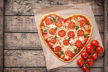 Heart shaped pizza margherita with tomatoes and mozzarella vegetarian meal on vintage wooden table...