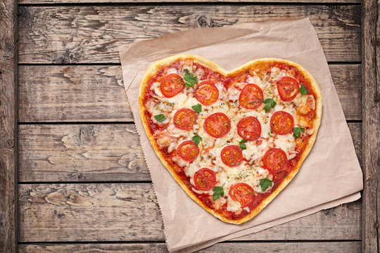 Heart shaped pizza margherita with tomatoes and mozzarella for Valentines Day on vintage wooden background. Food concept of romantic love.