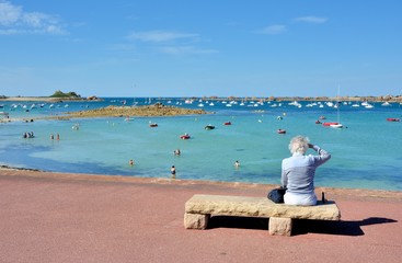 Une femme retraitée assise sur un banc de pierre regarde un beau paysage de mer