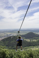 Teen going on a zip line adventure above a valley.
Teen boy going on a zip line adventure above a valley. Forest lay below and in the distance there are cultivated fields.