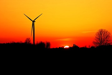 Obraz premium Wind Turbine Sunset horizon with a wind turbine and farm silhouette.