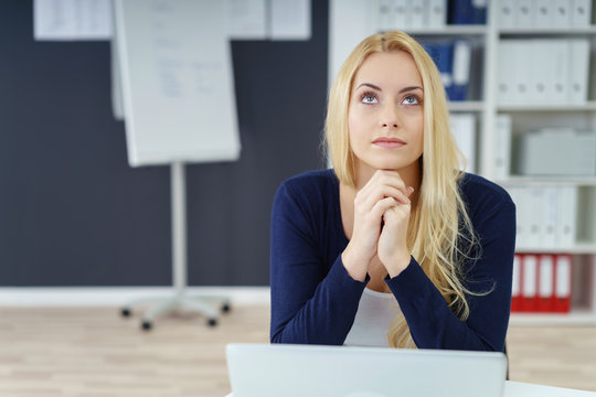 mitarbeiterin sitzt am schreibtisch und schaut in gedanken nach oben