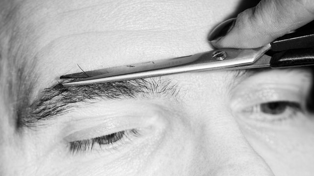 Portrait of man cutting eyebrow hairs.