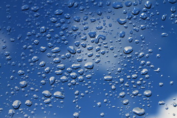 Rain drops on window with blue cloudy sky in background