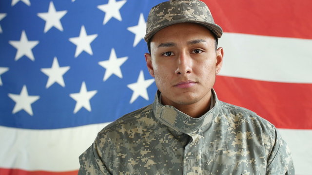 Portrait of Hispanic serviceman in fatigues standing in front of US flag