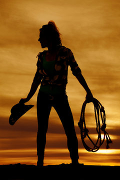 silhouette of a woman in an orange sunset holding cowboy hat and
