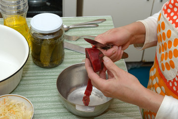 Top of cook table with hands of woman that peel the beetroot above small metal bowl.