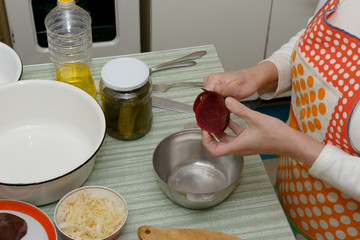 Top of cook table with hands of woman that peel the beetroot above small metal bowl.