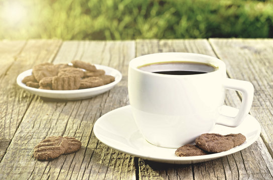 Cup of coffee on a wooden table with cookies. Natural background with sun lights and grass. Agriculture. Sweet and sugar.