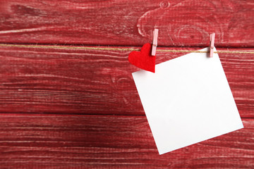 Blank paper hanging on rope on red wooden background