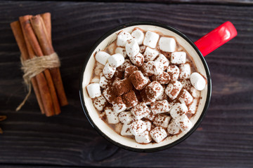 Cocoa with marshmallows in a red cup on a wooden table