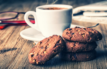 Cup of coffee with biscuit cookies and newspapper. Chocolate biscuit cookies. Chocolate cookies on white linen napkin on wooden table. Coffee break , breakfast.