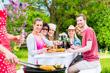 Mann bedient den Grill auf Gartenparty, seine Freunde essen das Grillgut