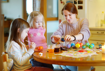 Young mother and her two daughters painting Easter eggs