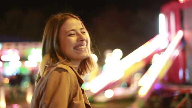 Young woman laughing and waving at camera in amusement park