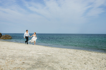 a young couple running at the beach, wedding at the sea, beautiful white wedding dress