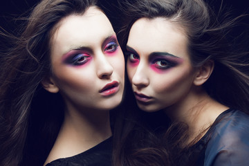Obraz premium Portrait of two beautiful young girls twins in the studio with bright makeup on a black background, the concept of beauty