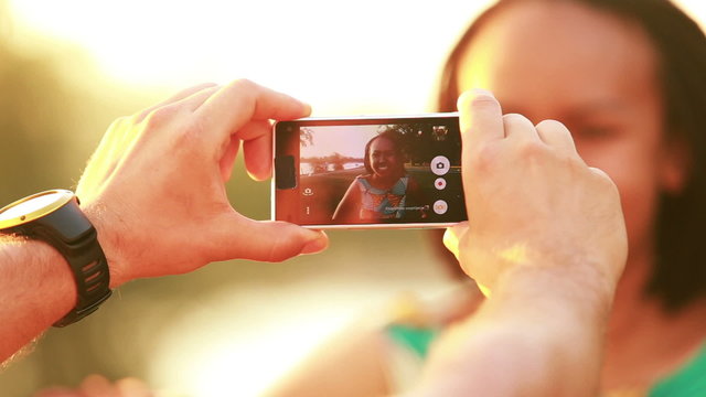 Young man taking pictures of beautiful woman with phone