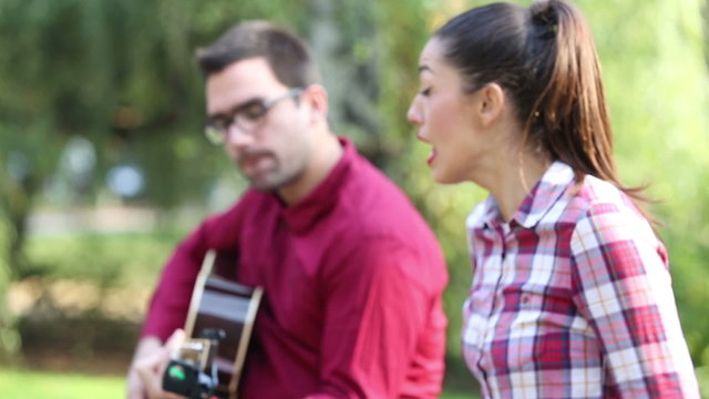 Young couple playing guitar and singing in park