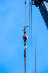 Weight with hook and chain hanging from crane on blue sky