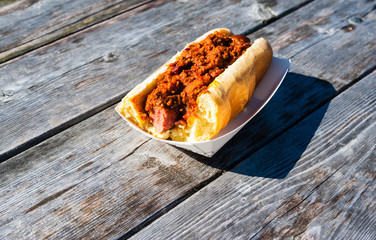 Partly eaten hot dog covered in chili on wood table