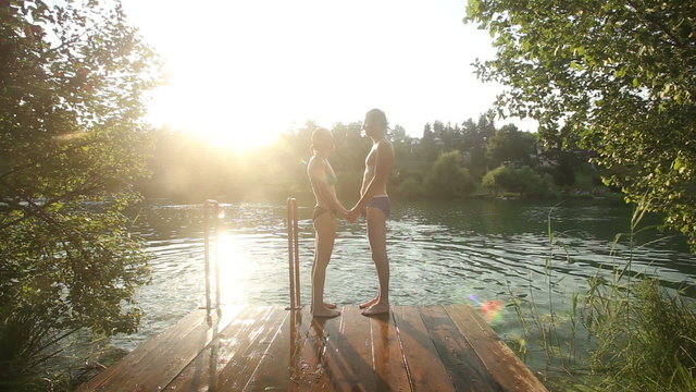 Couple in love standing on the dock holding hands by the river at sunset