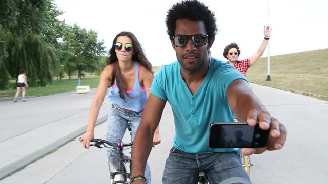 Three young adults having fun cycling and taking selfies