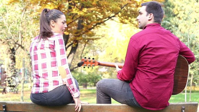 Man playing guitar while woman singing in park