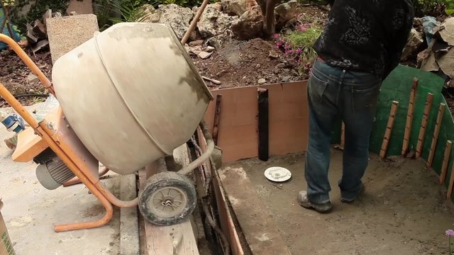 Video clip of mason taking fresh cement from the cement mixer during the construction of an artificial pond in ornamental garden.