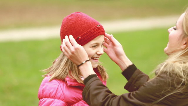 Mom putting cap on daughter's head and kissing her in forehead