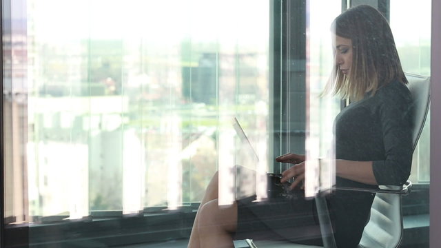 Beautiful businesswoman sitting on chair with laptop behind glass wall