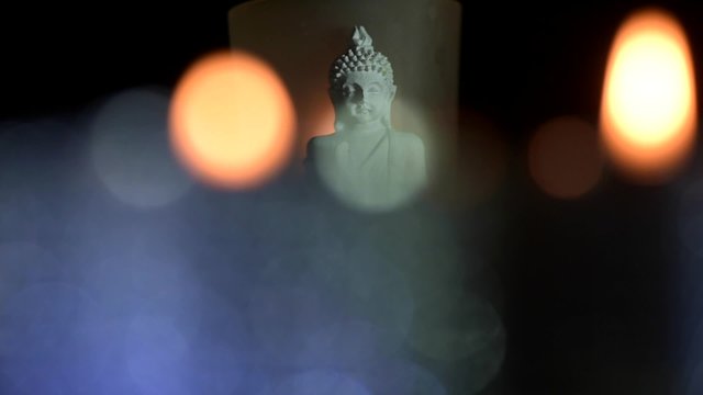 Buddha Statue With Lit Candle Against Black Background