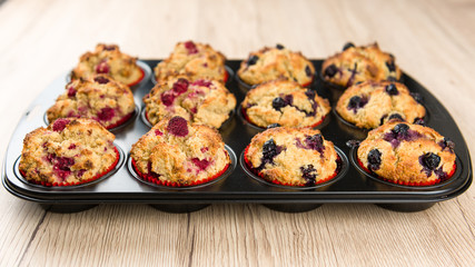 Black baking sheet with blueberry and raspberry cupcakes