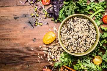 Wild rice with kale and vegetables ingredients for healthy cooking on rustic wooden background, top...