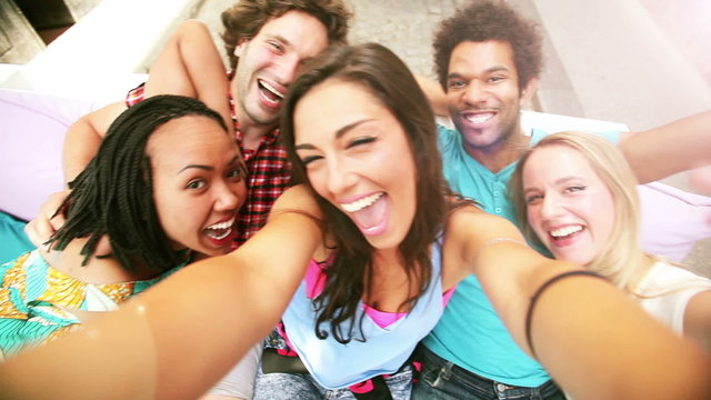 Five young adults laughing while taking a group selfie