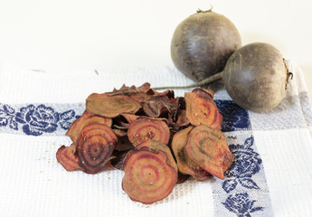     Thin round beetroot chips baked in the oven with oregano and salt and ripe beet roots in the white background. A healthy, vegetarian, vegan, crispy snack appetiser for diet and clean eating. 