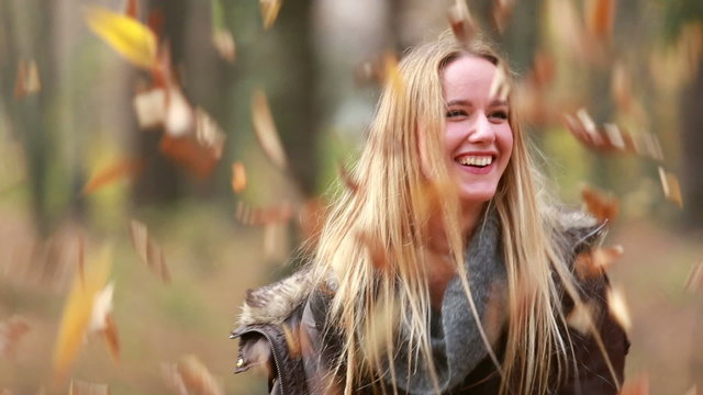 Young woman smiling and throwing leaves in the air