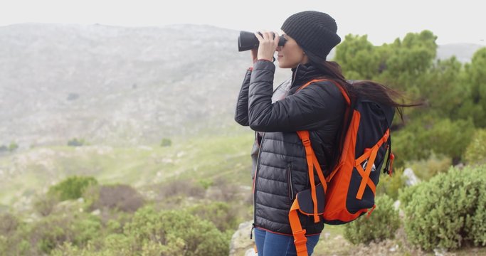 Young woman hiking in the mountain with her backpack on a misty cold day looking at the view through binoculars  side view